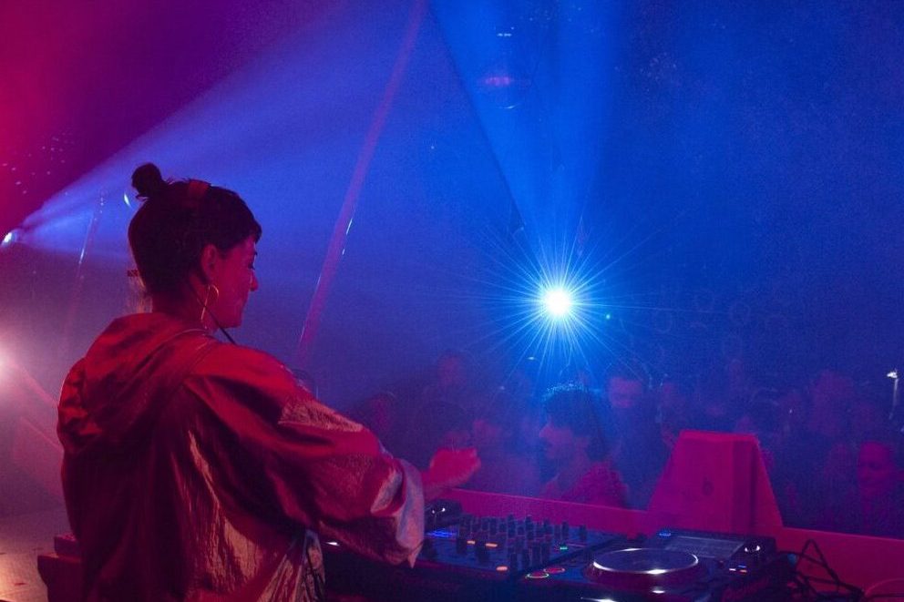 Foto mit DJ Monique Fessl an den Turntables, im Hintergrund Publikum