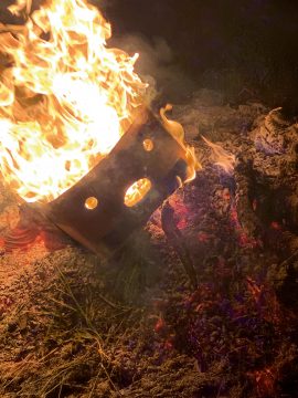 Foto mit einer brennenden Bananenkisten von der Seite, sieht aus wie ein Gesicht mit zwei Augen und einem Mund und Flammen ragen wie Haare aus der Kiste, aufgenommen in der Nacht