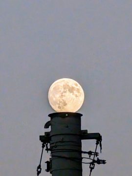 Foto mit einem Schornstein in der Dämmerung, darüber der Mond, der wie eine Kugel auf der Öffnung liegt